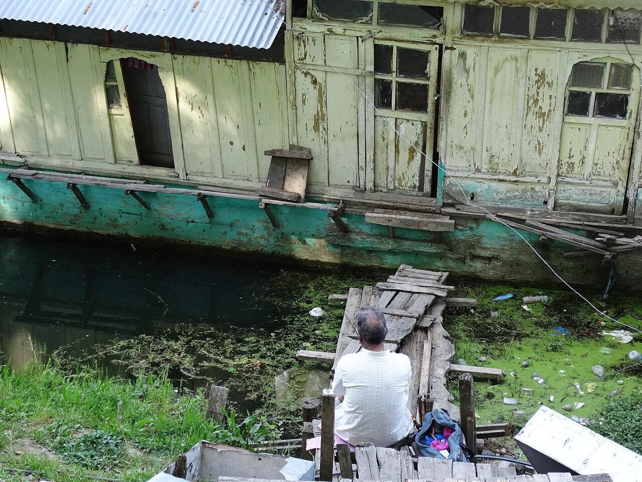 A man standing beside a wooden houseboat on Dal Lake in Srinagar