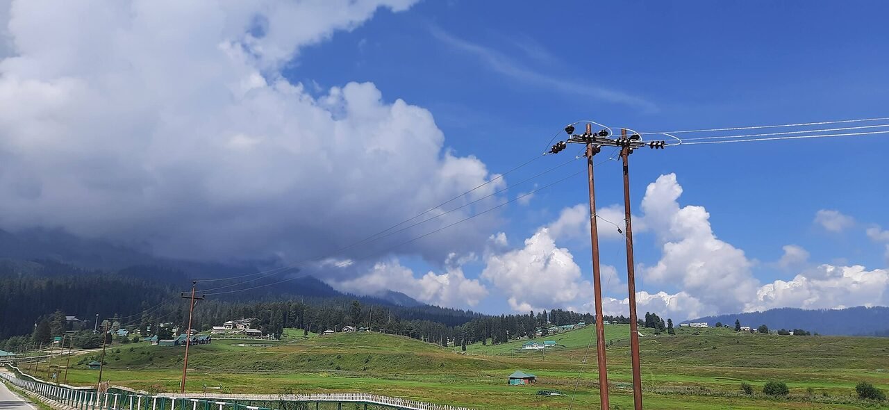 Bright green Gulmarg meadow with conifers and a walking path