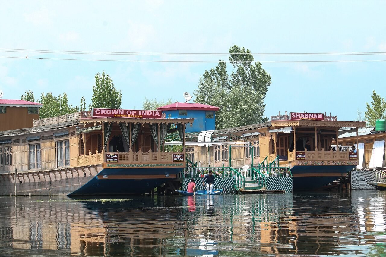 Wooden houseboats moored on Dal Lake in Srinagar, with trees and hills behind them